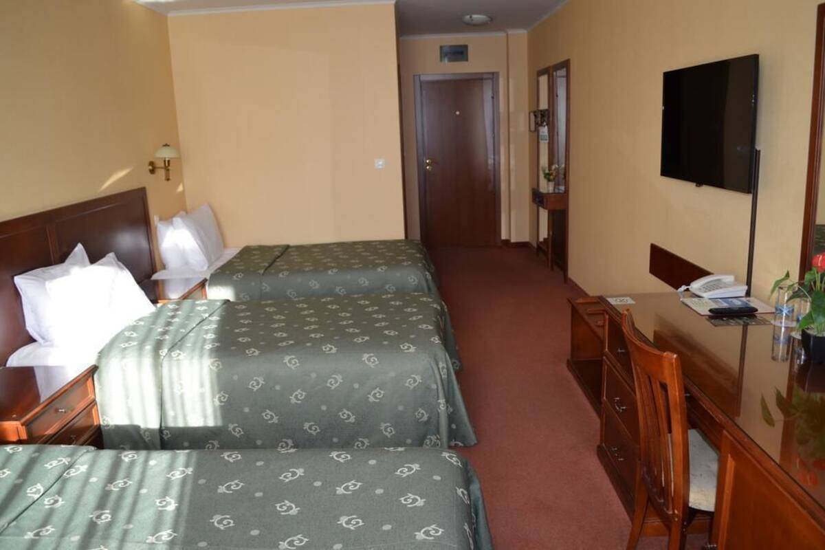 A hotel room with two beds, a desk, a chair, a TV, and a door.