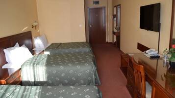 A hotel room with two beds, a desk, a chair, a TV, and a door.