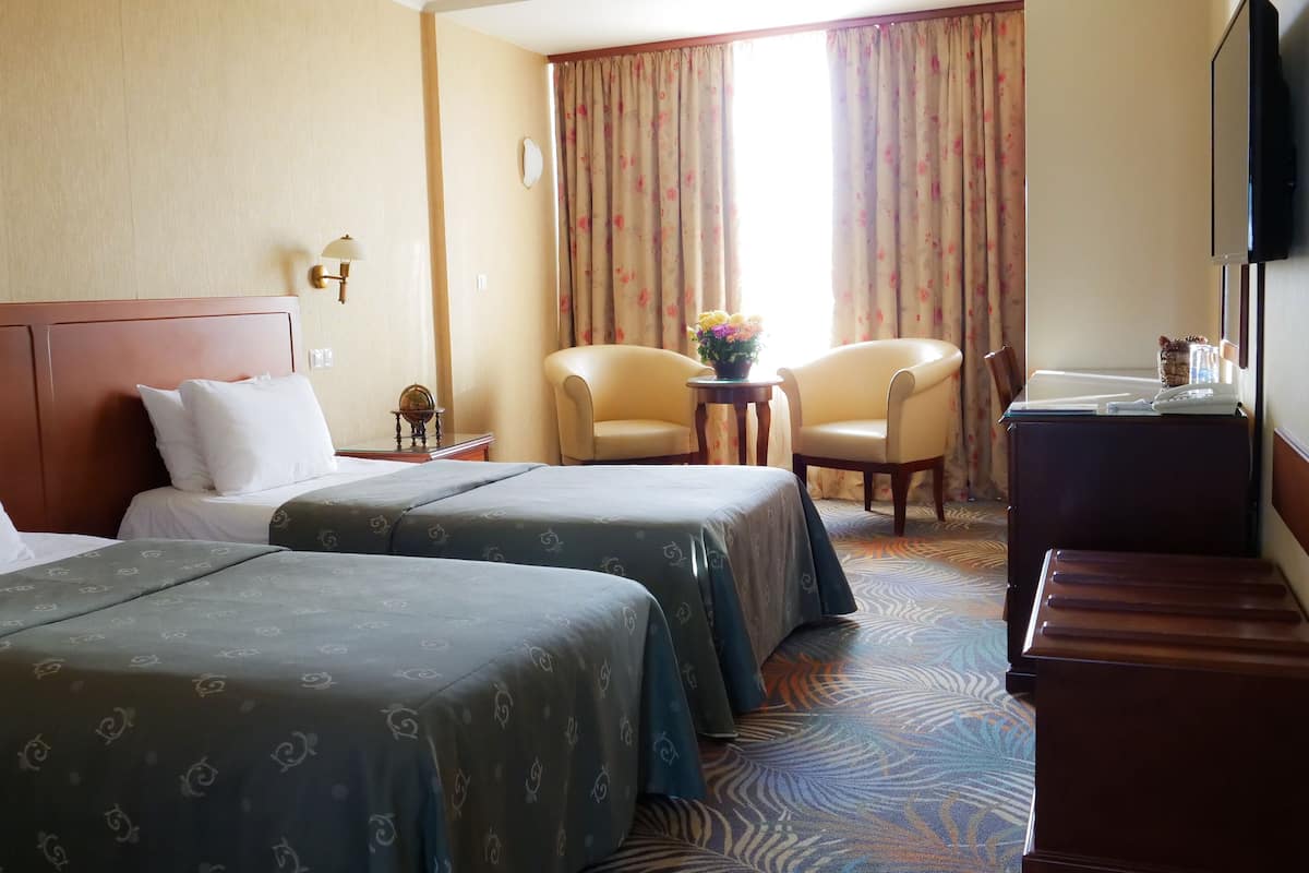 A hotel room with two beds, a desk, a chair, a TV, and a window with curtains.
