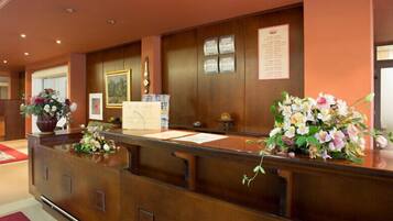 A reception desk with a wooden finish, a framed painting, and a bulletin board with notices.