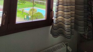 Quarto com uma janela grande com vista para uma piscina e vegetação.