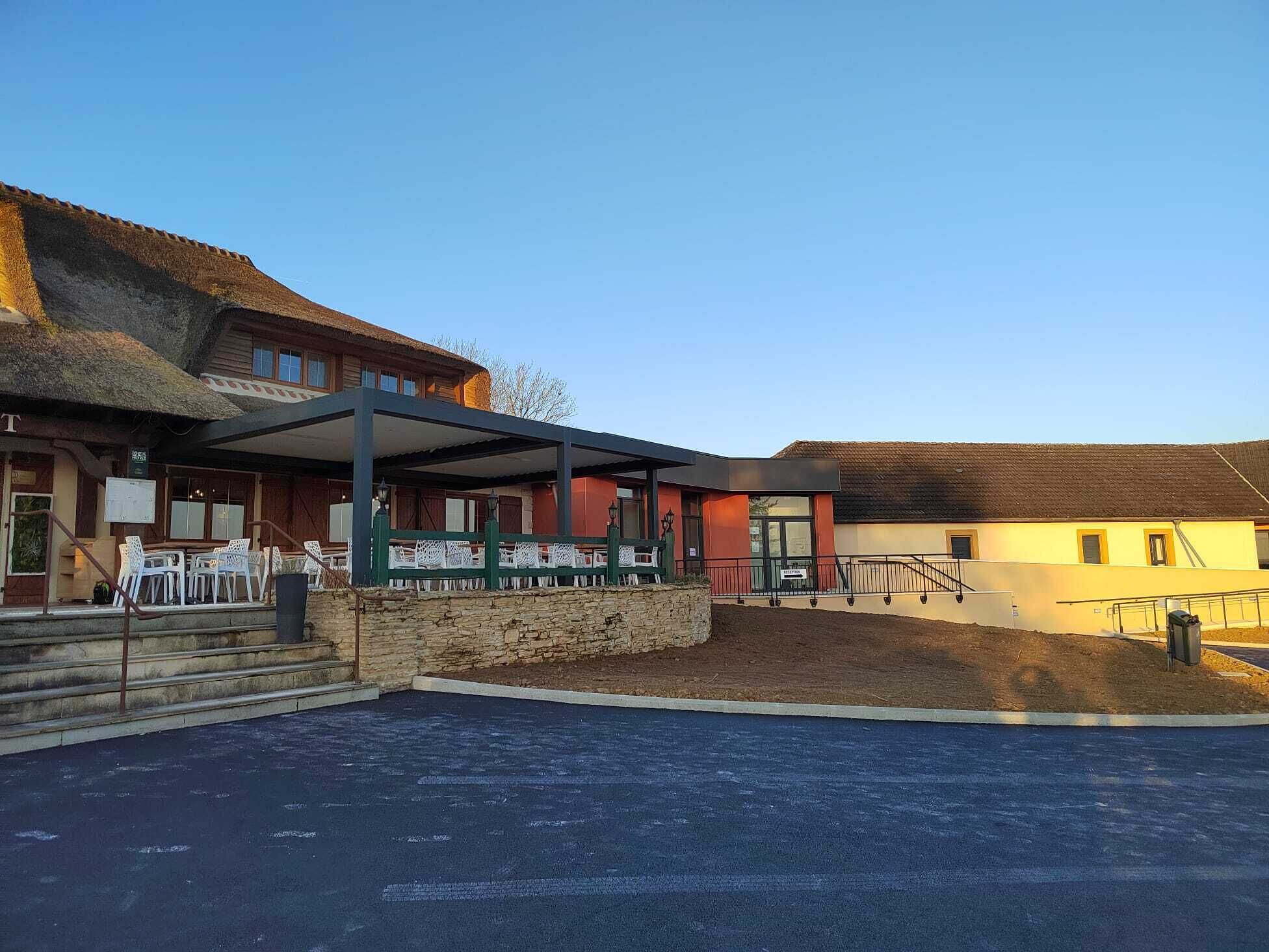 A building with a covered outdoor seating area, a stone wall, and a paved entrance.