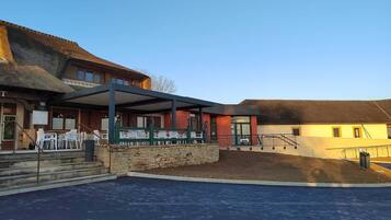 A building with a covered outdoor seating area, a stone wall, and a paved entrance.