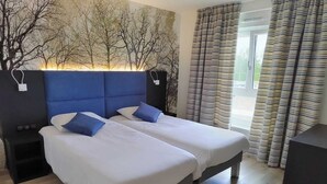 Quarto duplo com cama de casal, cabeceira azul, roupa de cama branca e duas almofadas azuis. Há uma mesa de cabeceira em cada lado da cama e uma janela com cortinas listradas.