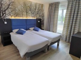 Habitación con cama doble, cabecera azul, ropa de cama blanca y dos almohadas azules. Hay una mesita de noche a cada lado de la cama y una ventana con cortinas a rayas.