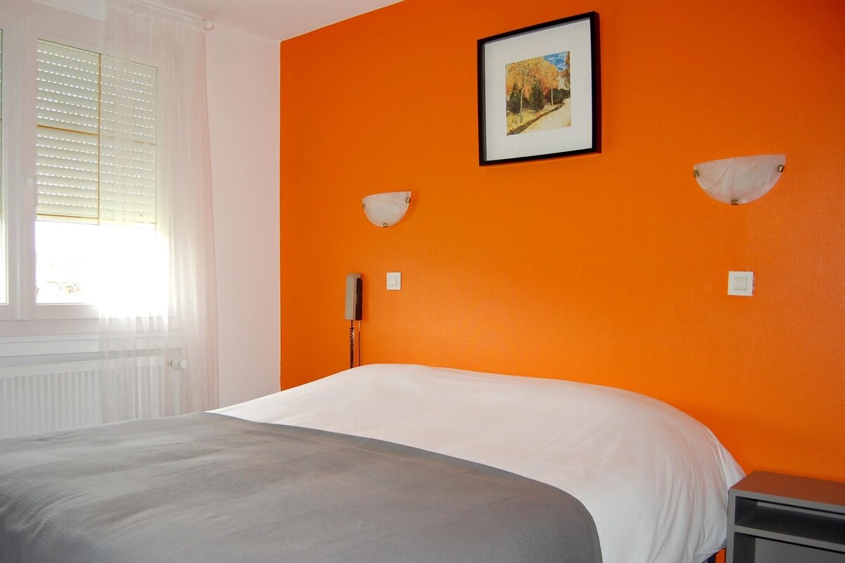 Une chambre à coucher comprenant un lit, une table de chevet, une commode, un tableau encadré au mur et une fenêtre avec des stores.