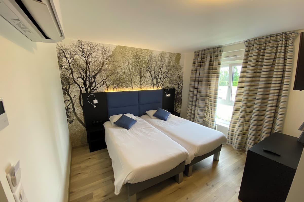 Een tweepersoonsbed met twee kussens, een hoofdeinde, een nachtkastje, een wandairconditioner en een raam met gordijnen.