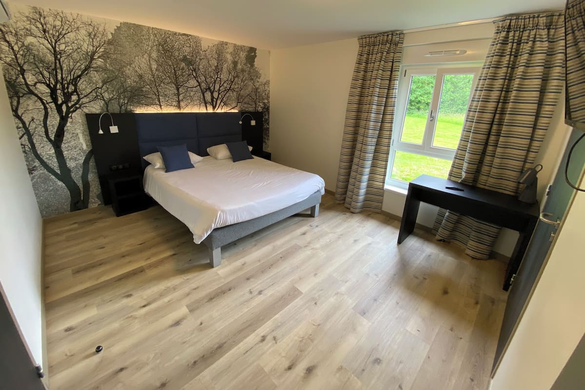 Een slaapkamer met een bed, nachtkastjes, een bureau en een raam met gordijnen.