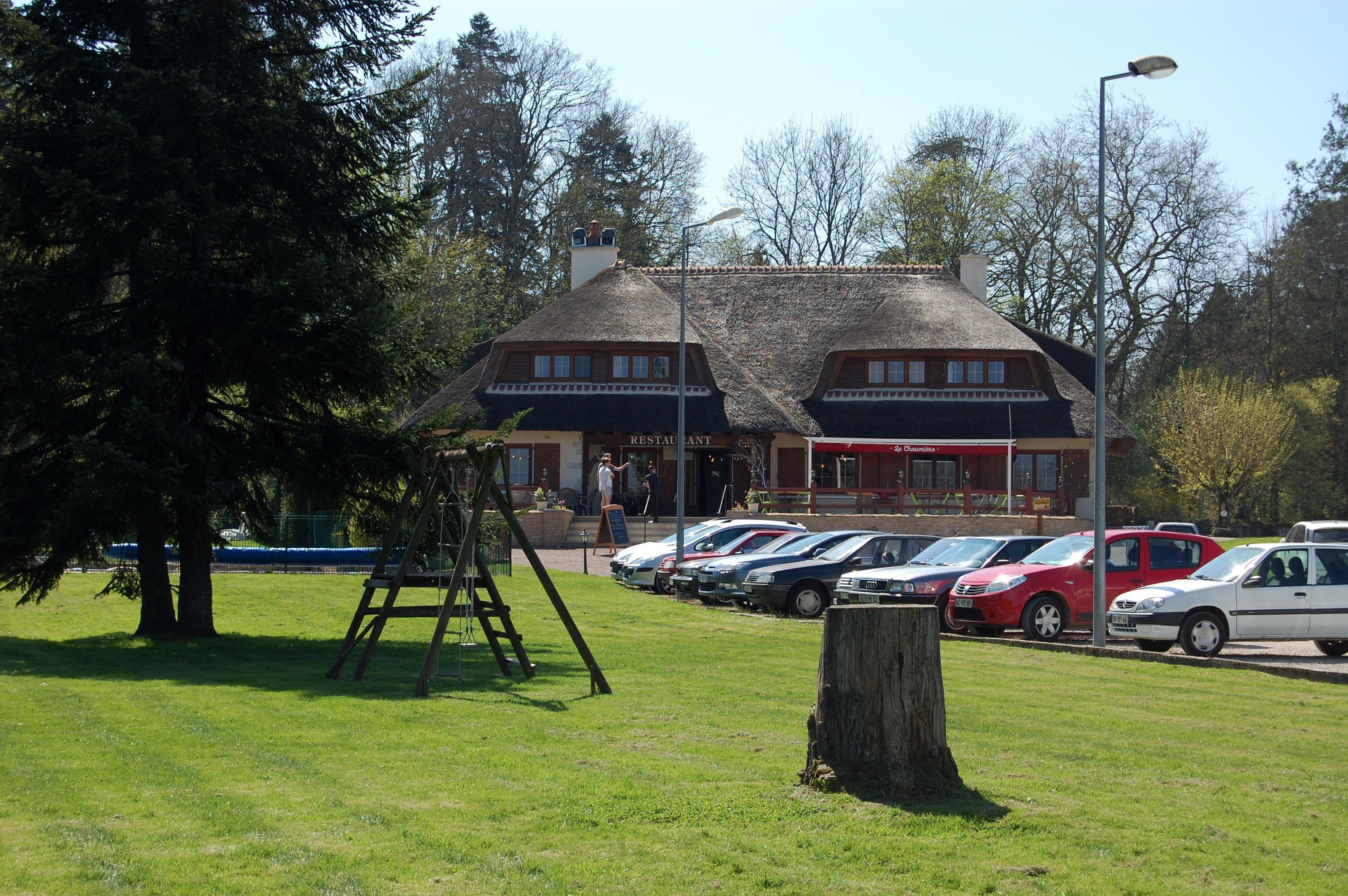 Un restaurant au décor traditionnel, un parking avec plusieurs voitures et un espace verdoyant avec des arbres.