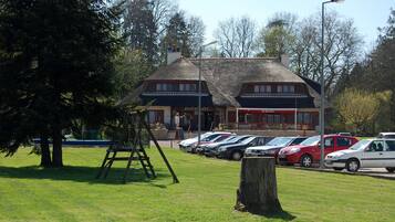 Un restaurant au décor traditionnel, un parking avec plusieurs voitures et un espace verdoyant avec des arbres.