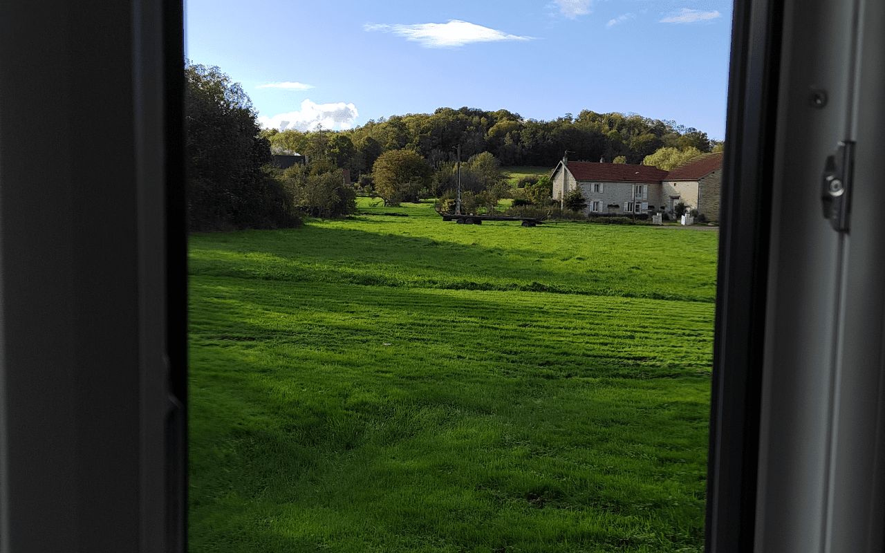 Vista a través de una ventana de un campo verde con una casa al fondo.