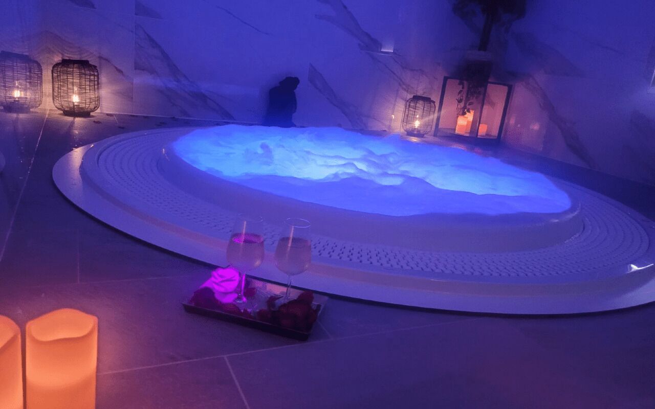 Zona de spa con hidromasaje, velas y una persona sentada junto a la bañera.
