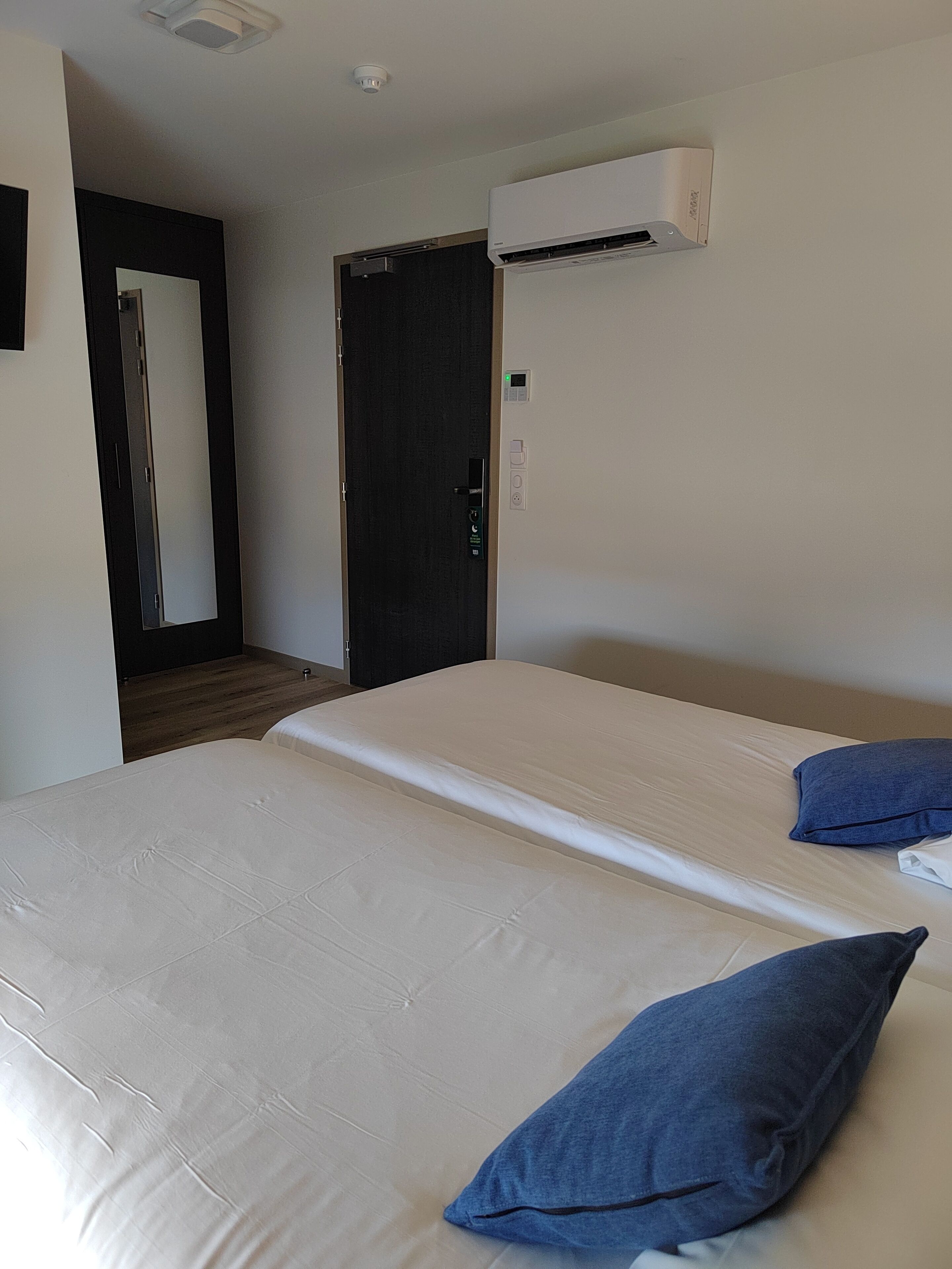 Quarto de hotel com cama, porta, ar condicionado e interruptor de luz.