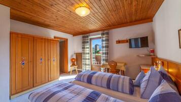 Une chambre avec deux lits, un plafond en bois, un bureau, une chaise, une télévision et une vue sur l’extérieur.