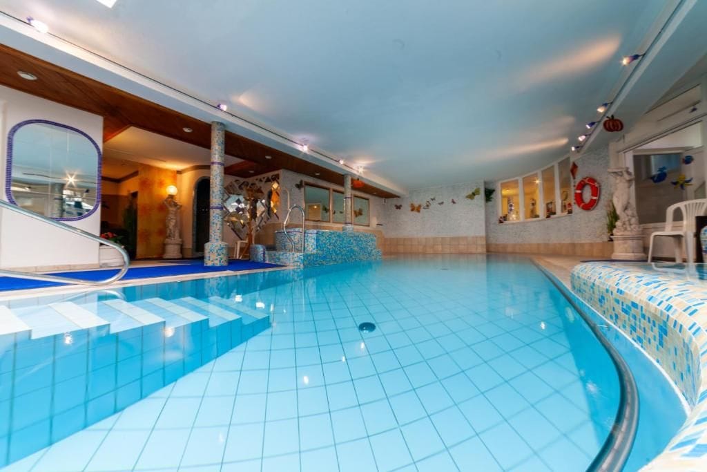 An indoor swimming pool with a tiled floor, a lifebuoy on the wall, and a chair near the pool.