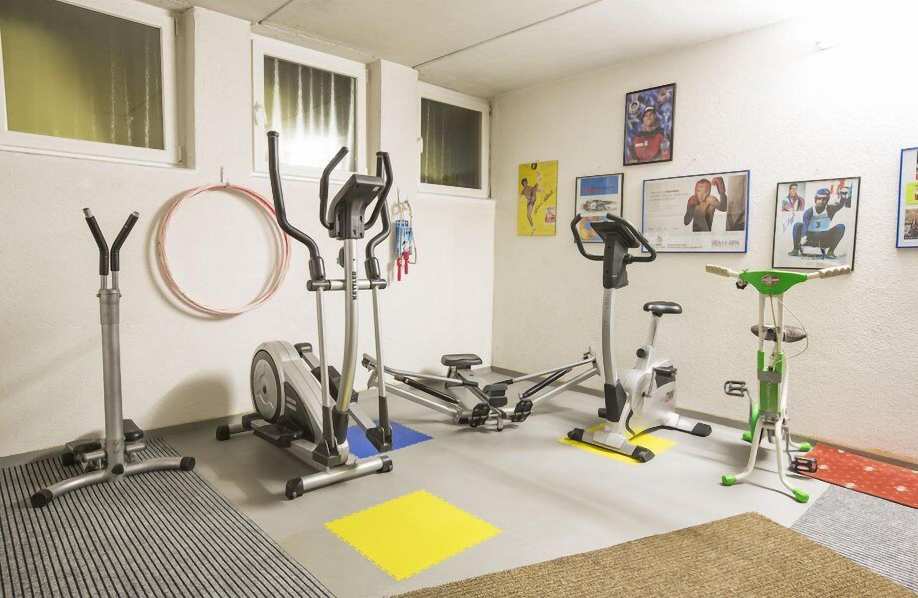 Ein Fitnessraum mit verschiedenen Trainingsgeräten, darunter ein Ergometer, ein Crosstrainer und ein Rudergerät.