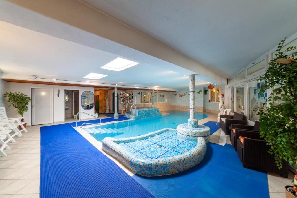 Ein Innenpool mit blauem Mosaikstreifen, einer Fontäne und Sitzbereichen mit Pflanzen.