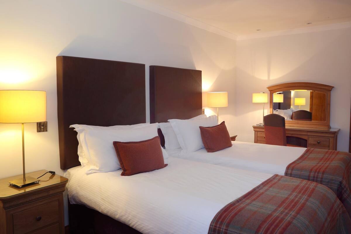 A hotel room with a large bed, two bedside lamps, a wooden nightstand, a dresser, and a mirror.