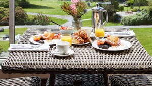 Una mesa de desayuno con cruasanes, fruta y jugo, con vista a un lago y un bosque.