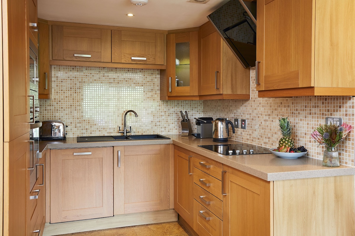 Una cocina con armarios de madera, salpicadero de azulejos, electrodomésticos de acero inoxidable y un frutero sobre la encimera.
