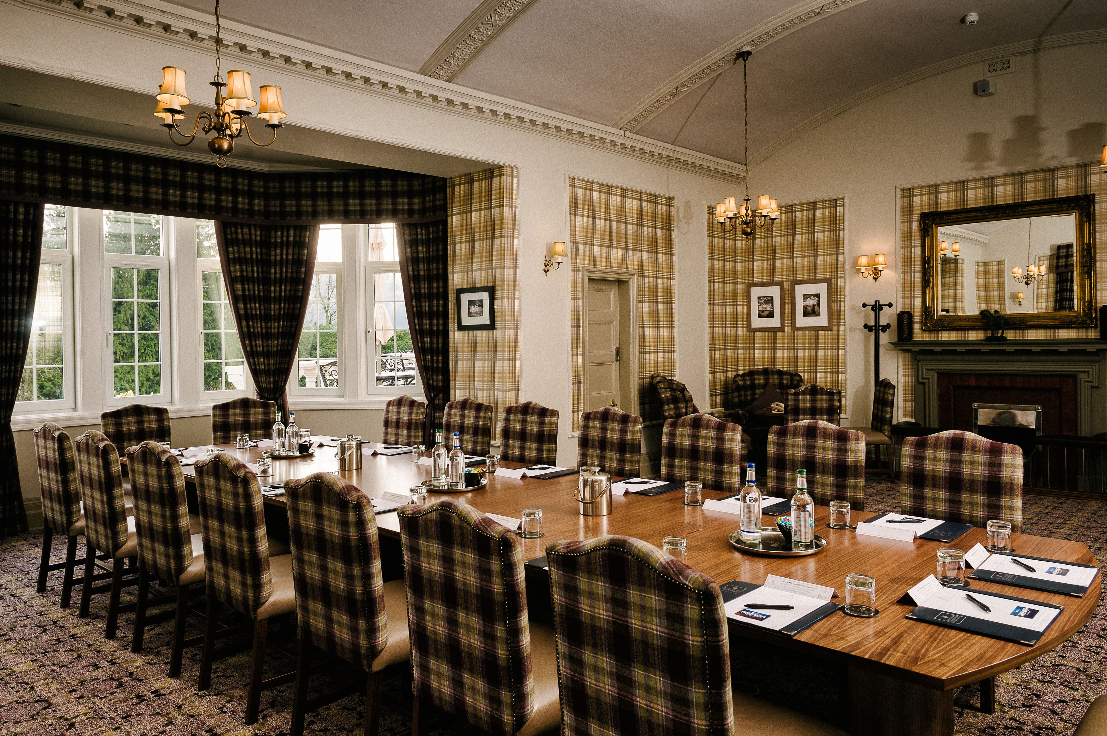 A conference room with plaid chairs, a large wooden table, and a fireplace.