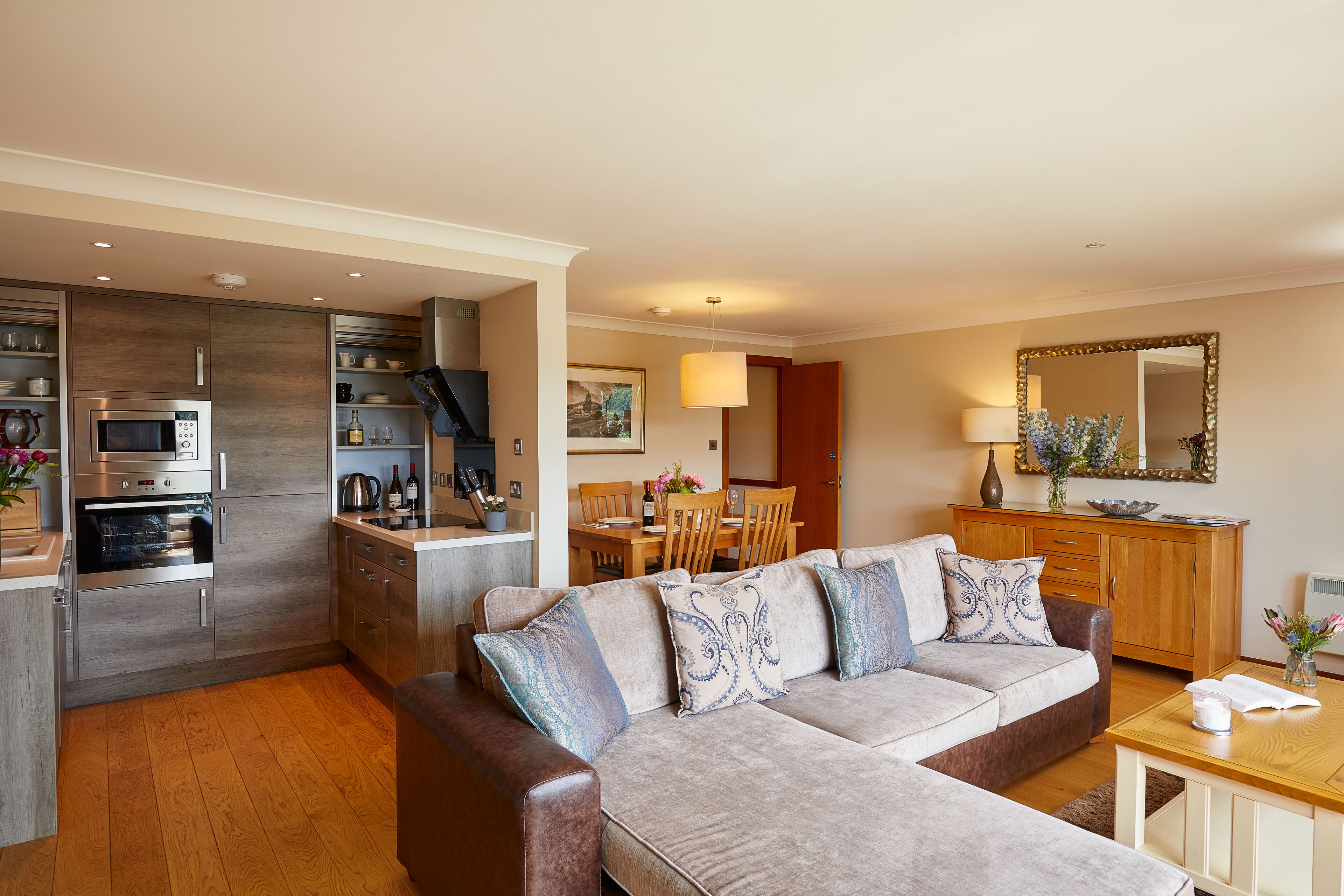 A modern kitchen with a built-in oven and microwave, a dining area with a wooden table and chairs, and a living room with a sofa and a coffee table.
