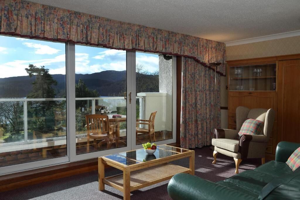 Una sala de estar con vistas a montañas, un comedor con sillas, una mesa con fruta y un sofá verde.