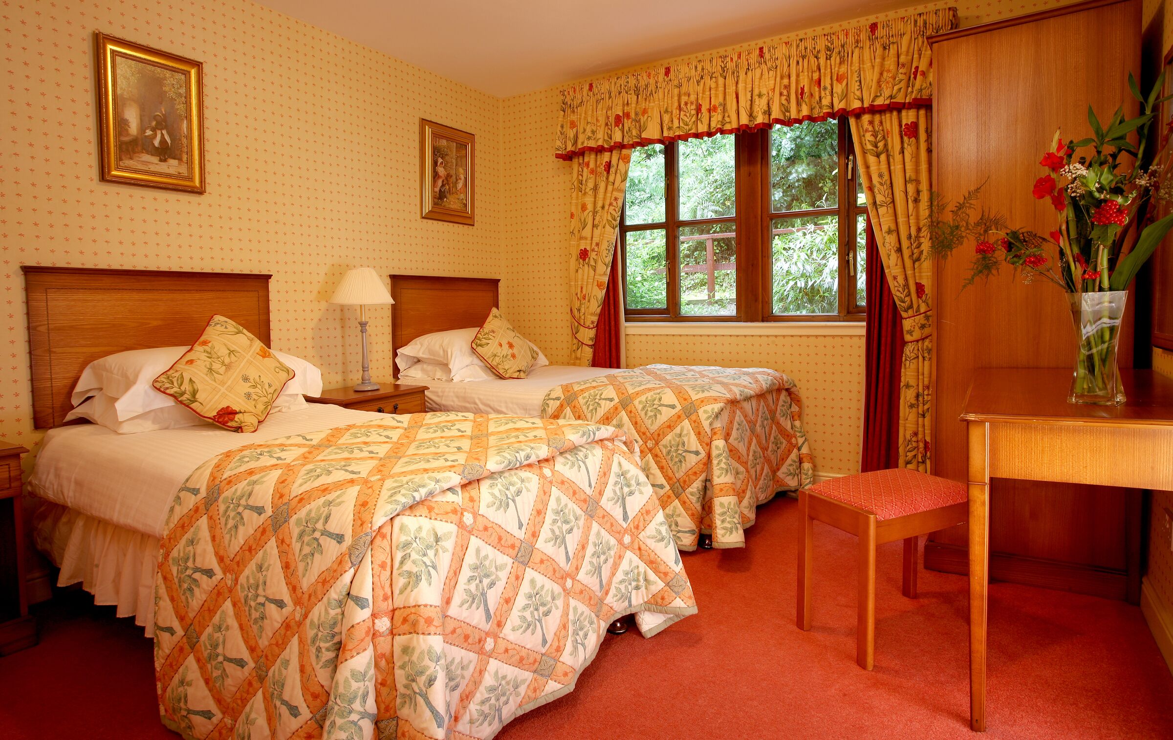 Een kamer met twee bedden, een nachtkastje, een bureau en een raam met gordijnen.