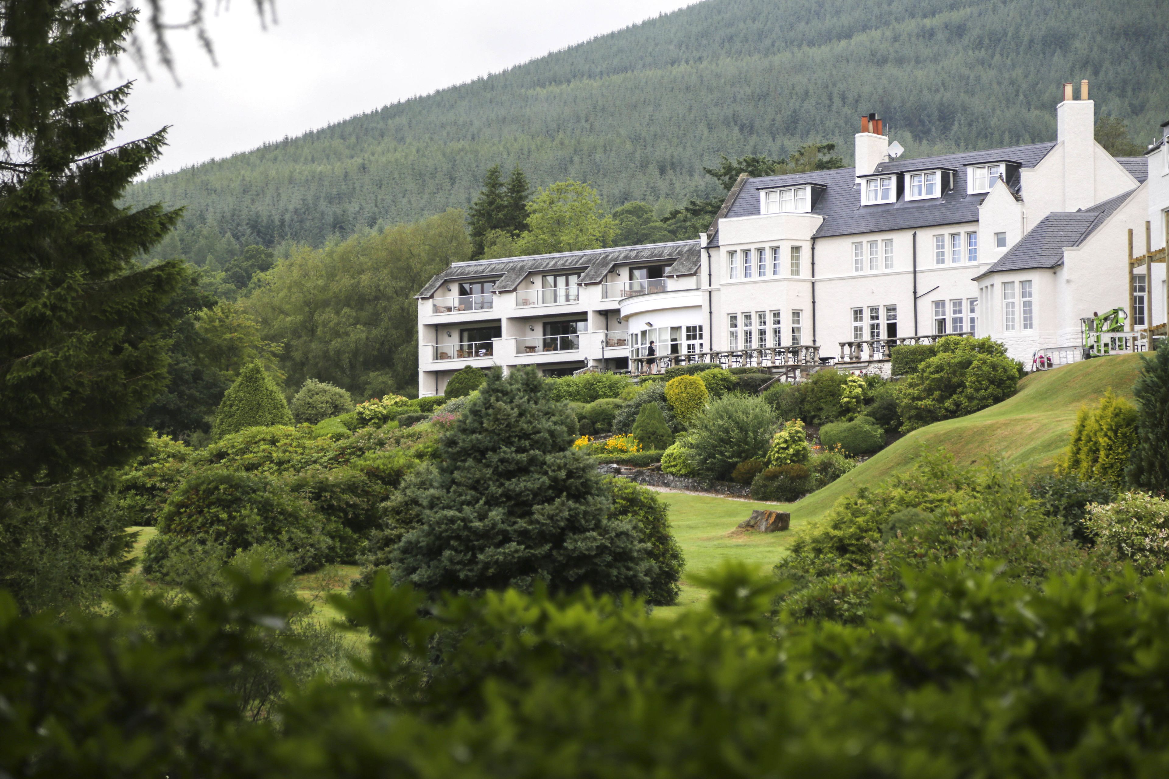 A large, multi-story hotel with a landscaped garden and a view of a forested hill.