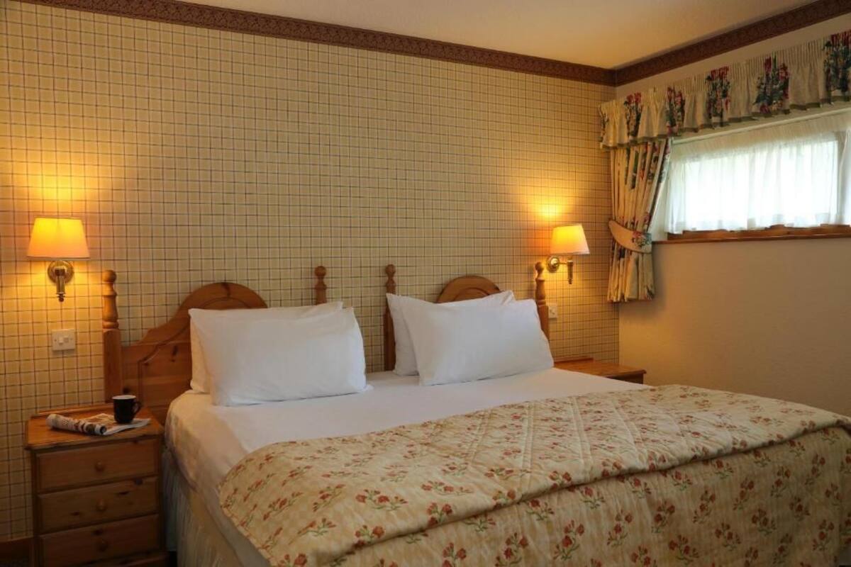 A neatly made bed with white linens, two bedside lamps, and a floral-patterned bedspread.
