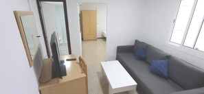 A room with a grey sofa, a white table, a wooden desk, a mirror, and a wardrobe. - Hostal El Mercat (Villajoyosa)