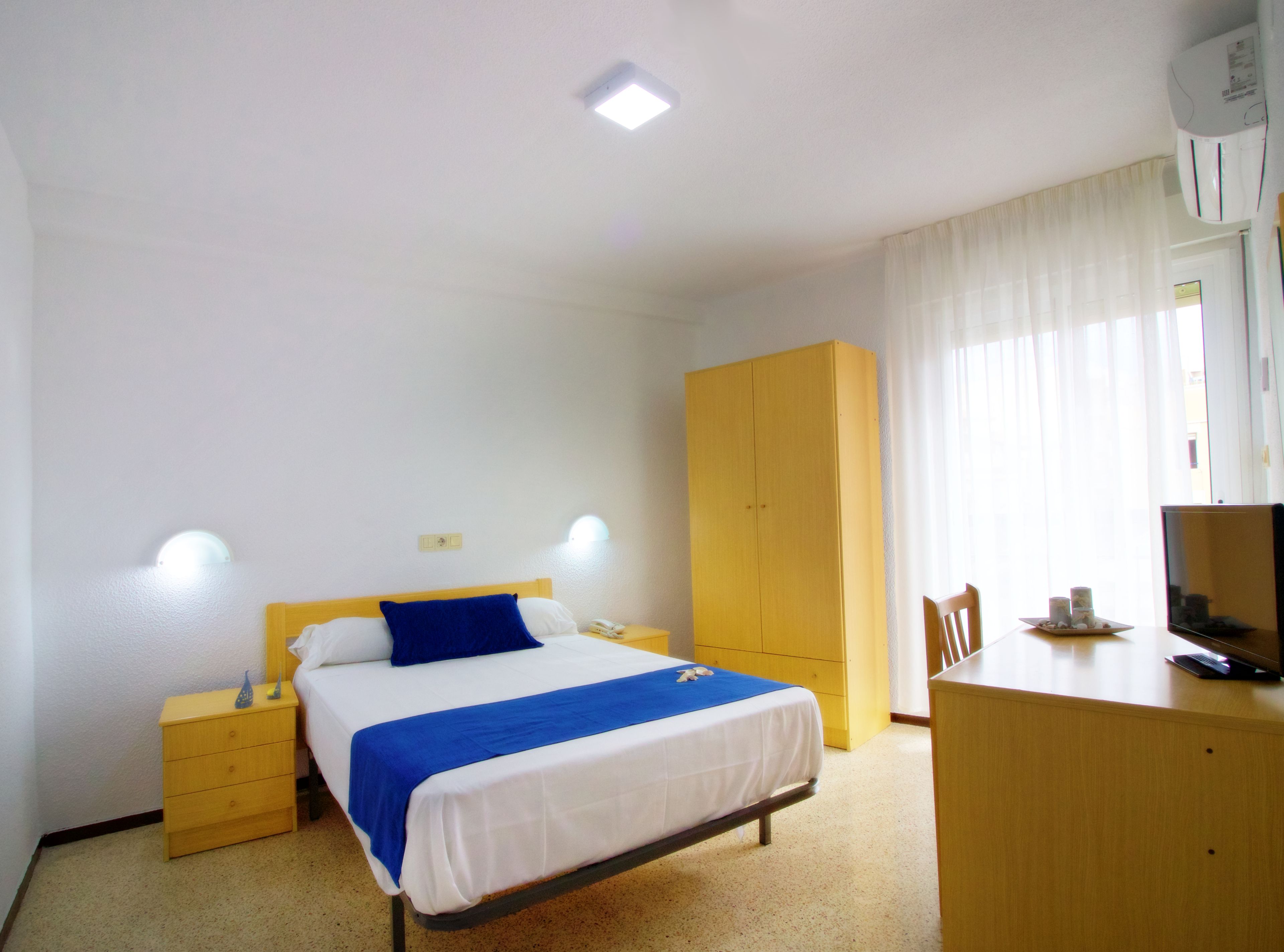 Una habitación de hotel con cama, escritorio, armario y televisor.