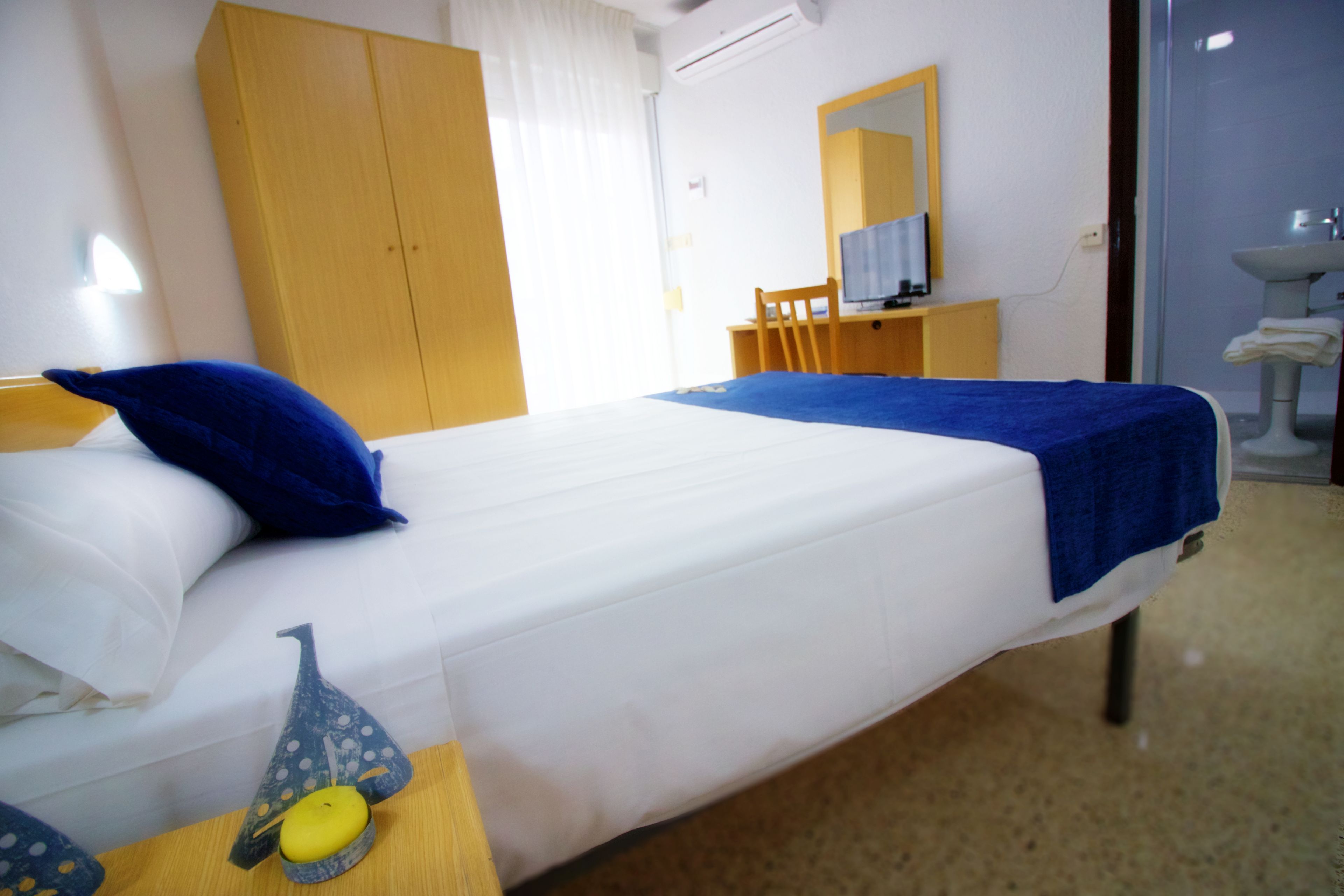 A hotel room with a bed, a desk, a chair, a television, and a bathroom with a sink and mirror.