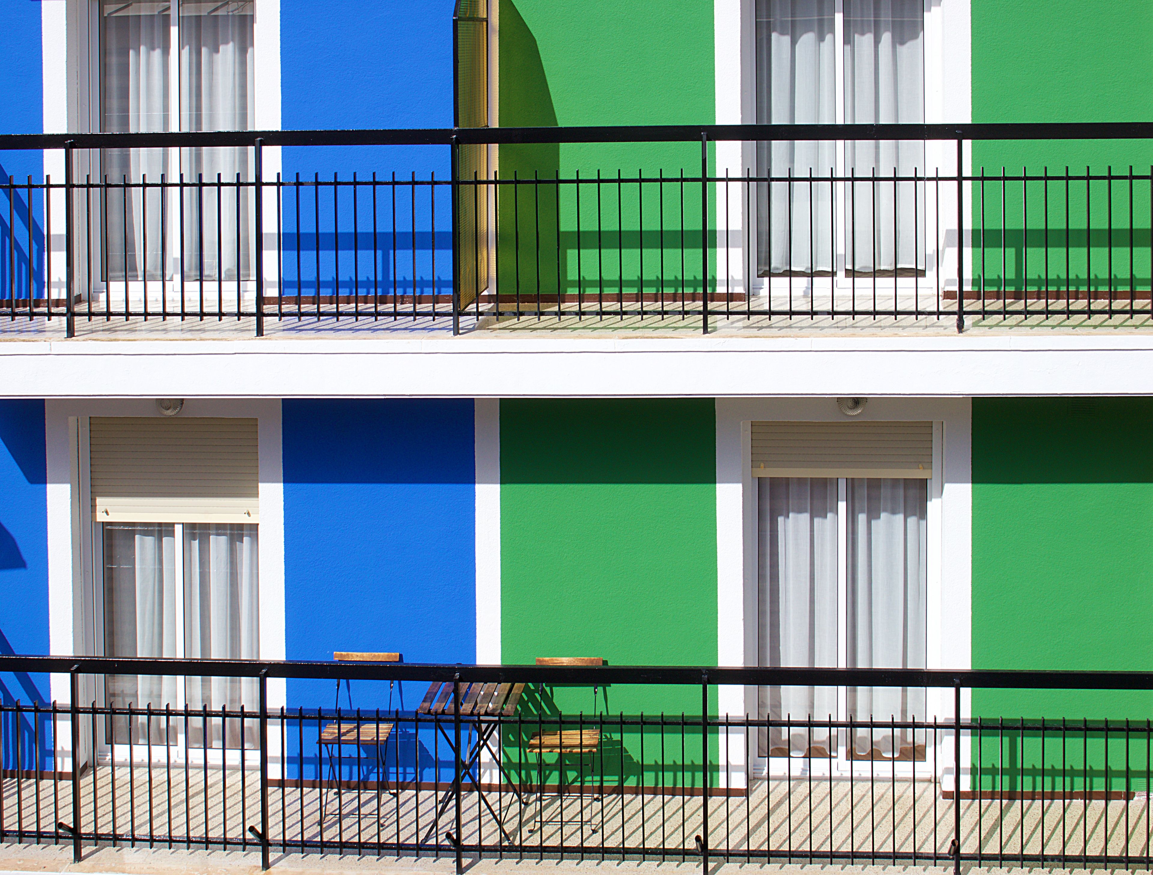 Un edificio de dos pisos con balcones, cada uno con barandilla de metal y una ventana con cortinas blancas.