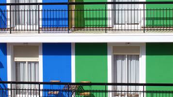Un edificio de dos pisos con balcones, cada uno con barandilla de metal y una ventana con cortinas blancas.