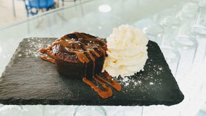 A dessert on a slate plate with a caramel drizzle and a scoop of vanilla ice cream. - Hostal El Mercat (Villajoyosa)
