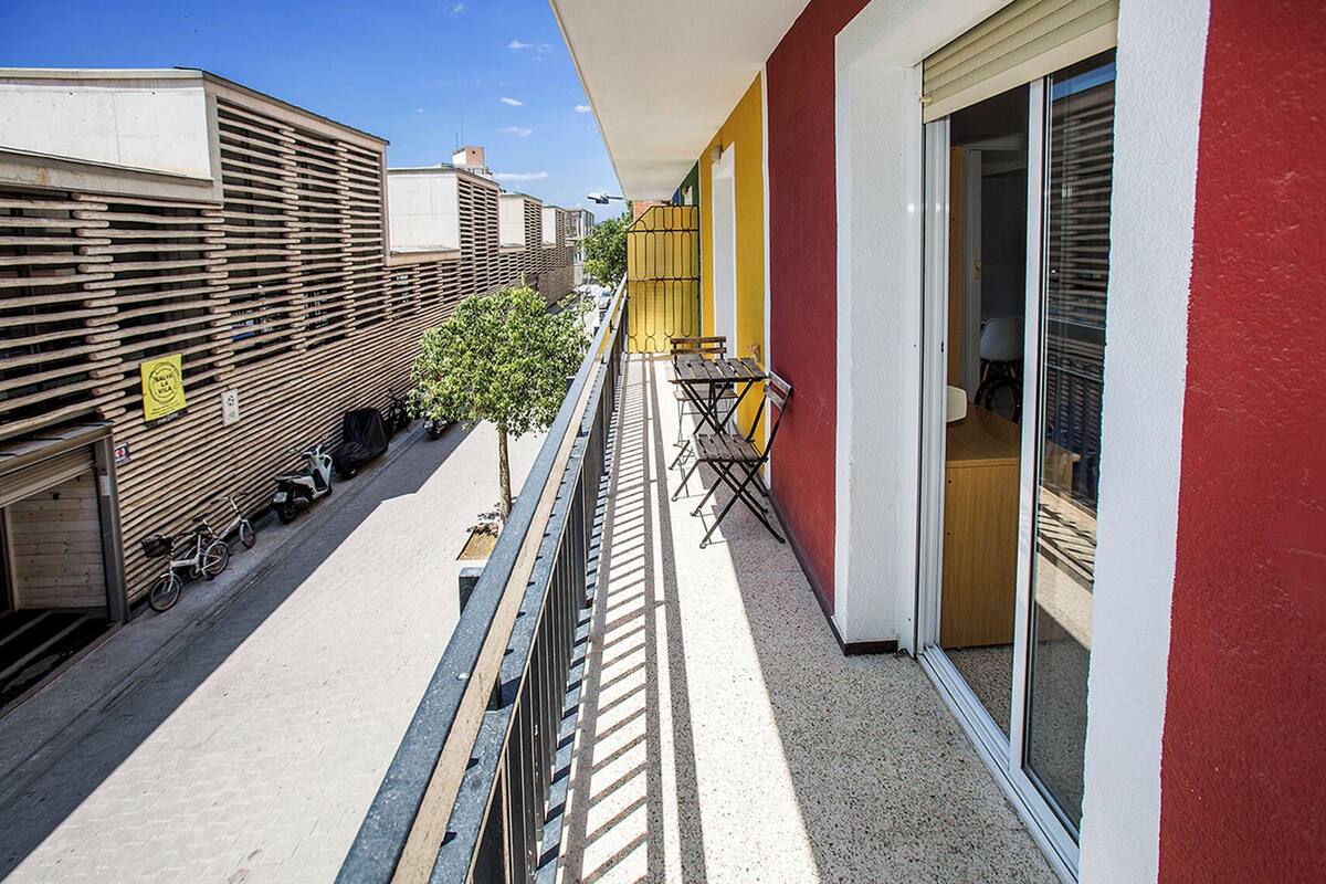 Un balcón con vistas a bicicletas y scooters estacionados, un pequeño árbol y una mesa con sillas.