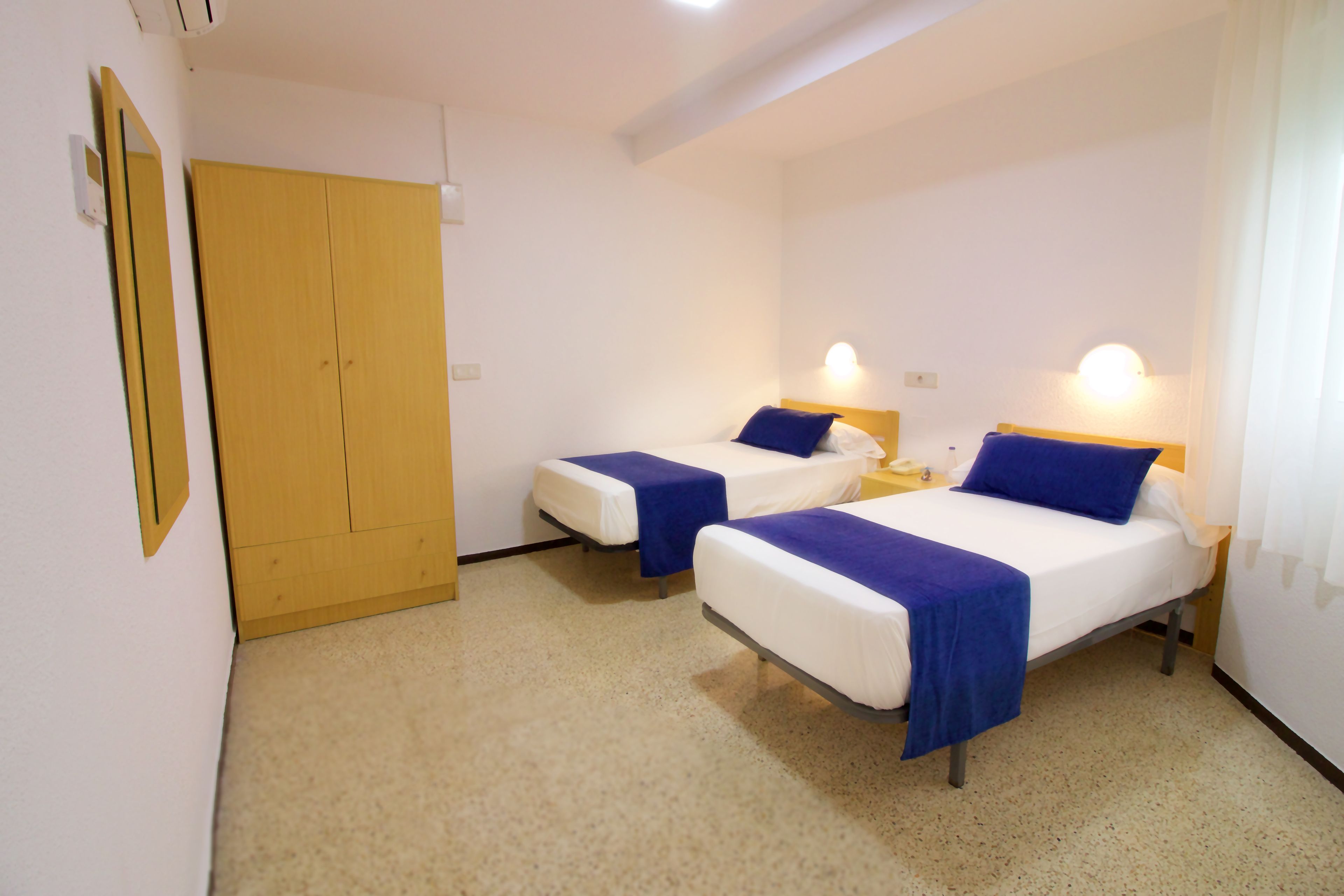 Ein Hotelzimmer mit zwei Einzelbetten, einem Holzschrank und einem kleinen Nachttisch mit Lampe.