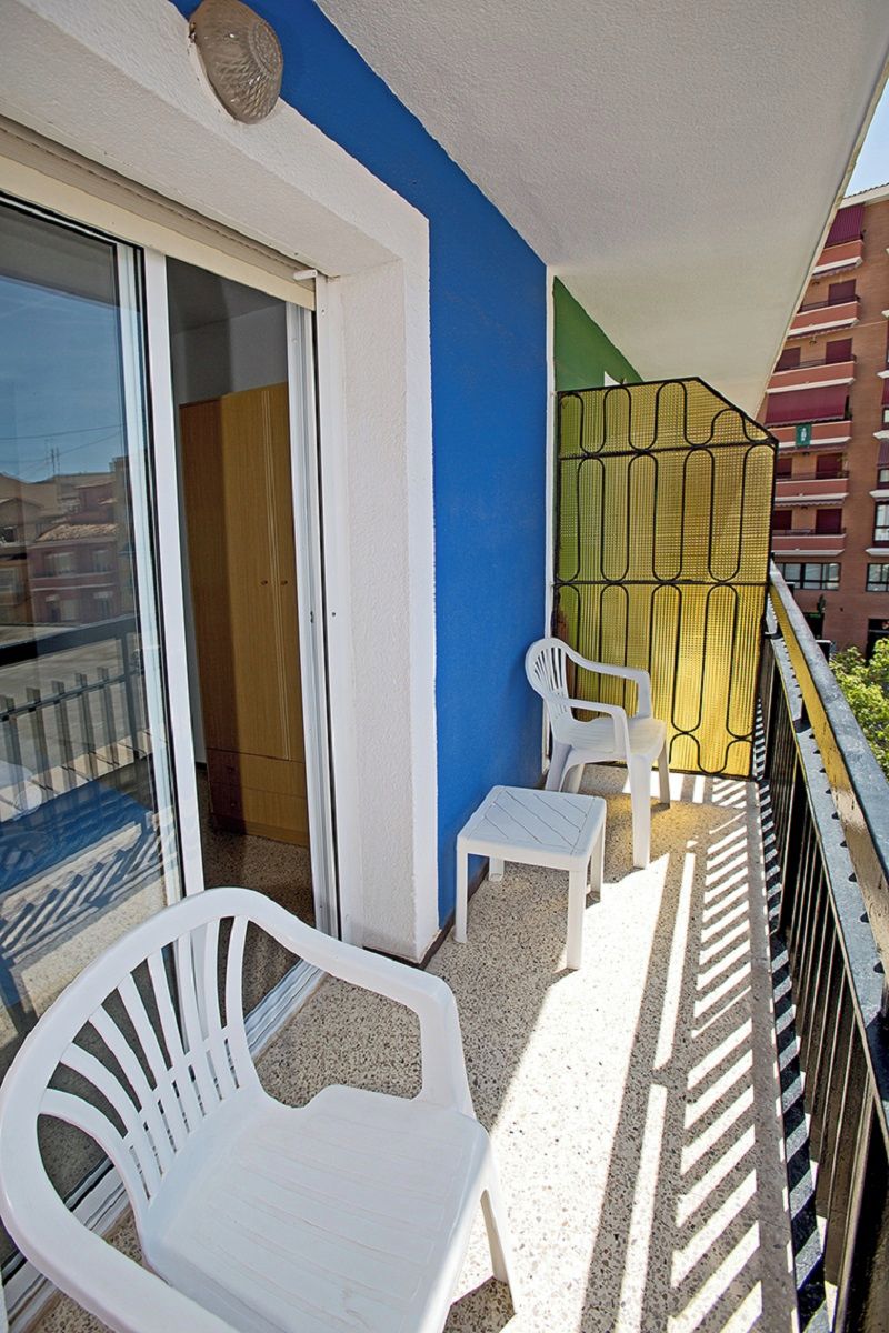 A balcony with two white plastic chairs, a glass door, and a green patterned wall.
