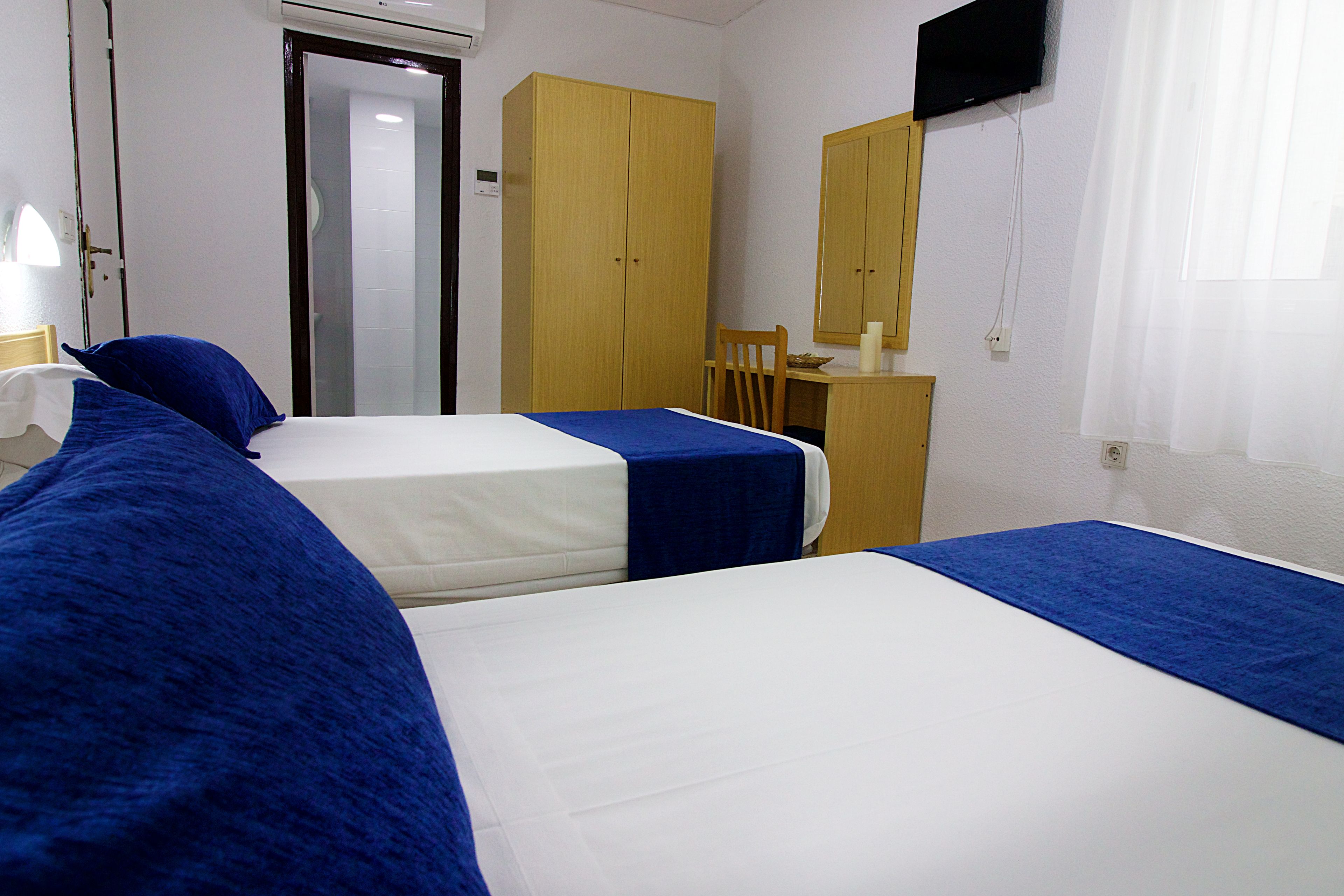 Habitación de hotel con dos camas, un armario de madera, un escritorio con silla y un televisor en la pared.