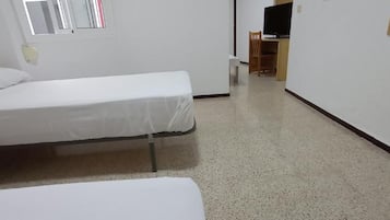 Una habitación con dos camas individuales, un escritorio con silla y un televisor.