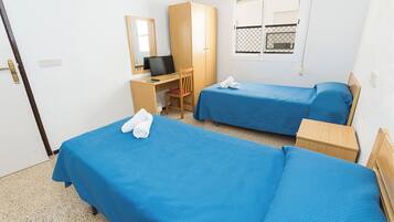 Une chambre d’hôtel avec deux lits simples, un bureau avec une chaise, un ordinateur et une fenêtre donnant sur l’extérieur.