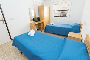 Habitación de hotel con dos camas individuales, un escritorio con silla, una computadora y ventana con vista al exterior.