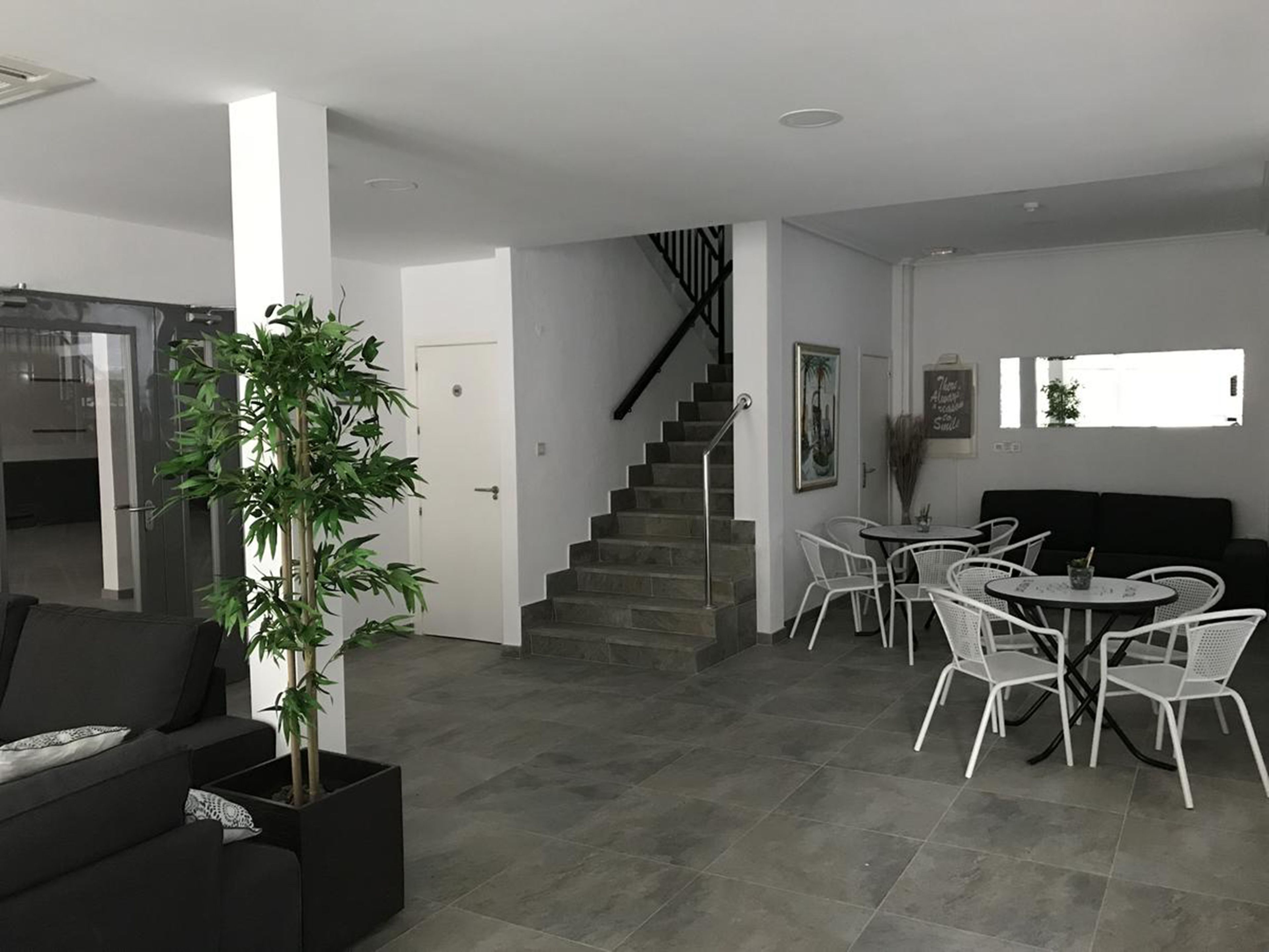 Una sala de estar moderna con una escalera, un comedor con sillas blancas y un sofá negro.