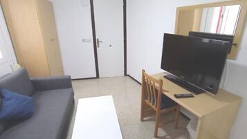 Una habitación con un sofá, una televisión sobre un mueble bajo, una mesita y una puerta.