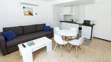 Un salon moderne avec un canapé gris, une table basse blanche et un coin repas avec des chaises blanches.