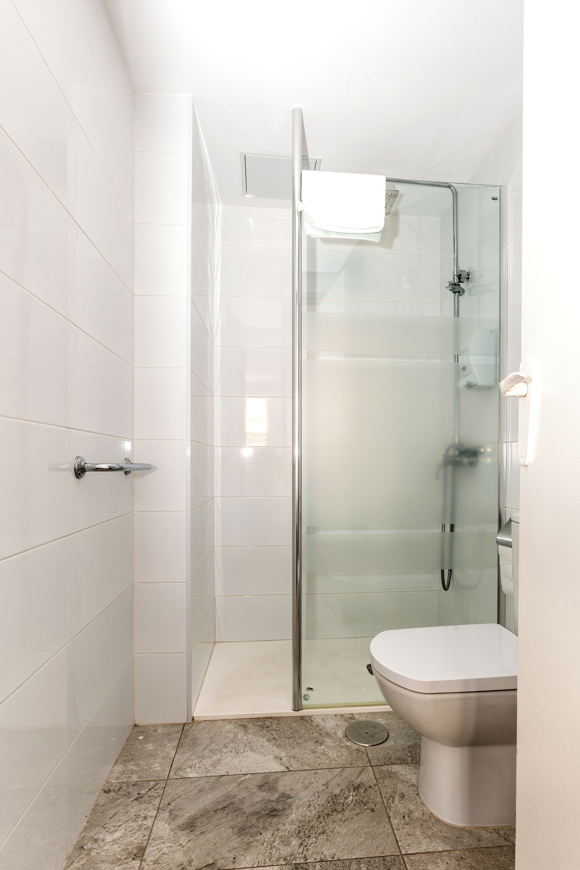 A modern bathroom with a glass shower enclosure, a toilet, and a tiled floor.