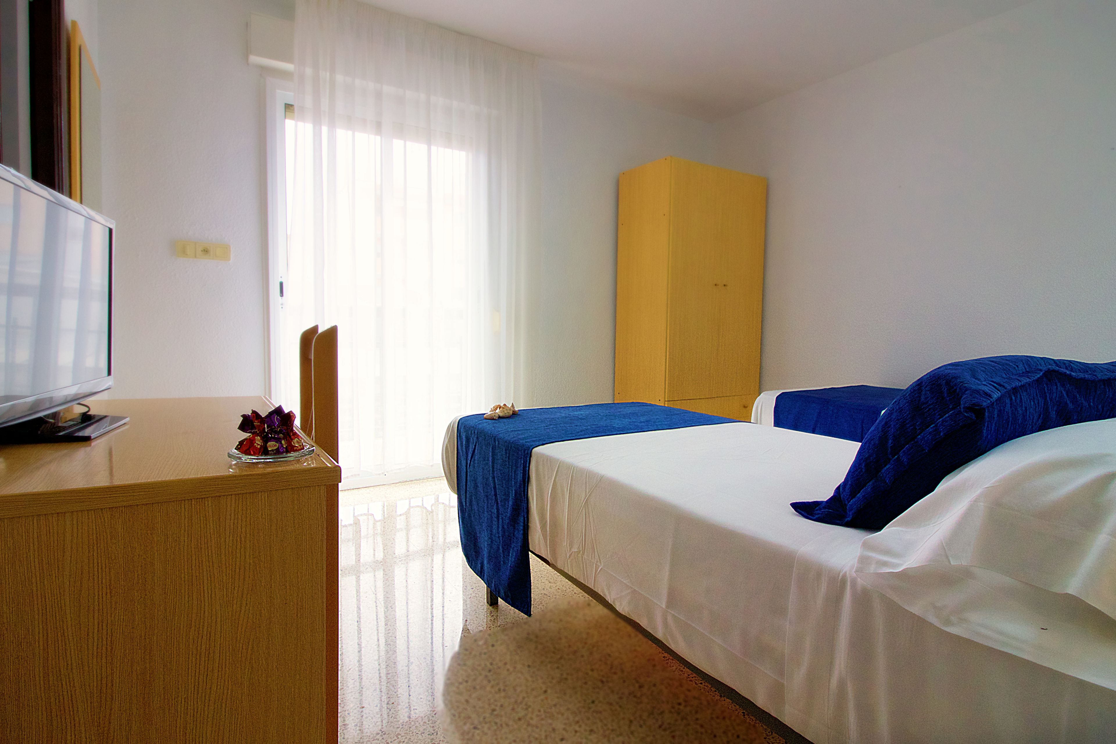 Una habitación de hotel con cama, escritorio, televisión y ventana con cortinas.