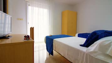 Una habitación de hotel con cama, escritorio, televisión y ventana con cortinas.