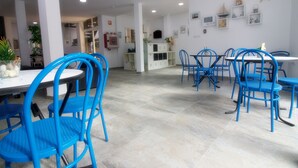 A spacious dining area with blue chairs and a white table, featuring a tiled floor and white walls with decorative items. - Hostal El Mercat (Villajoyosa)